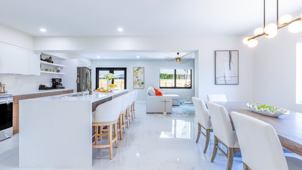 A modern kitchen with a central island, white cabinetry, and a dining area with a wooden table and white chairs. - Welcome to Casa Luna – Your Private Oasis with Heated Pool! (Cutler Bay)