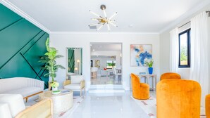 Una sala de estar moderna con un sofá blanco, sillones naranjas y una planta grande.