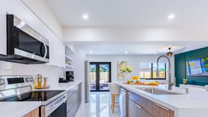 A modern kitchen with a microwave, stove, and dishwasher. There is a bar area with a sink and a ceiling fan. - Welcome to Casa Luna – Your Private Oasis with Heated Pool! (Cutler Bay)