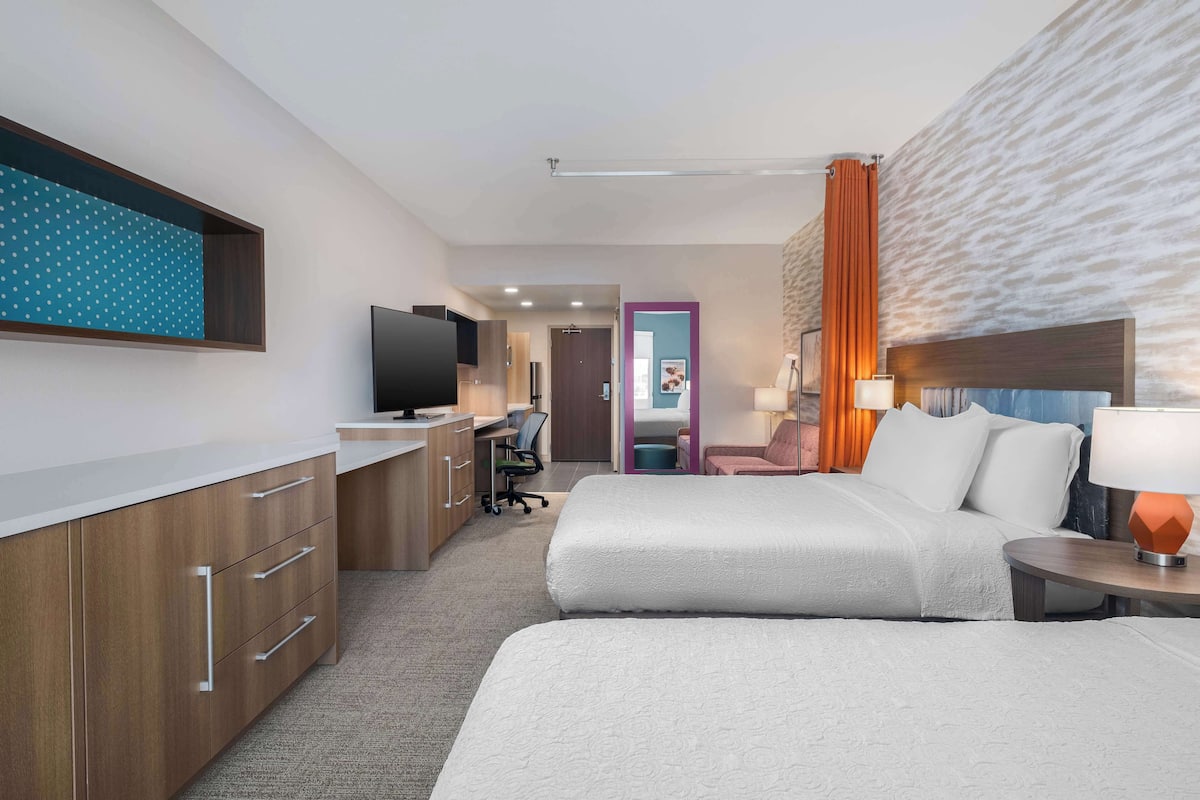 A hotel room with a bed, bedside table, lamp, TV, desk, chair, and a wardrobe.