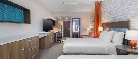 A hotel room with a bed, bedside table, lamp, TV, desk, chair, and a wardrobe.