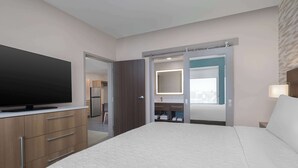 Habitación de hotel con una cama grande, televisión de pantalla plana, armarios de madera, baño con espejo y un armario con puerta corredera.