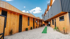 A modern building with wooden and metal exterior walls, a paved walkway, and small potted plants. - Bungalow (Tbilisi)