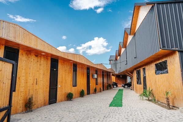 Un edificio moderno con paredes exteriores de madera y metal, un sendero pavimentado y pequeñas macetas con plantas.