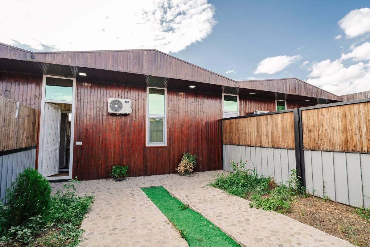 Un bâtiment moderne à l’extérieur en bois, doté de grandes fenêtres et d’une cour pavée agrémentée d’une bande de verdure.