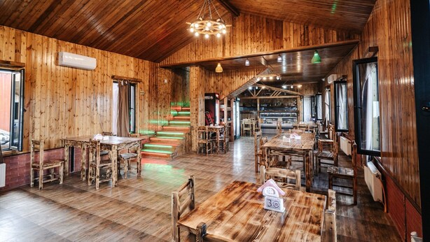 A spacious wooden interior with multiple dining tables and chairs, a staircase, and a bar area. - Bungalow (Tbilisi)