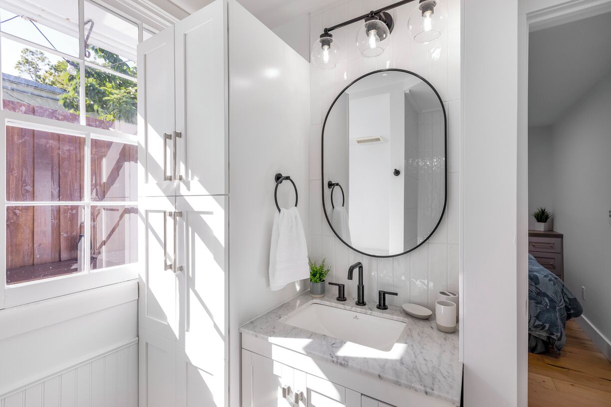 Un baño con tocador blanco, un espejo grande y una ventana.
