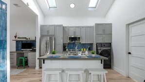 Ett modernt kök med grå skåp, en köksö med barstolar, en inbyggd tvättmaskin och ett takfönster.