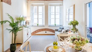 A cozy living room with a brick arch, large windows, a dining area with a table set, and a sofa. - Paolino View Apartment (Lucca)
