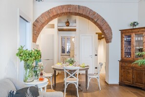 A dining area with a brick archway, white chairs, a round table set with plates, glasses, and a vase of flowers. - Paolino View Apartment (Lucca)