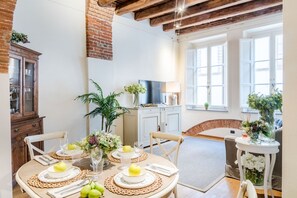 A dining area with a round table set for four, surrounded by chairs. There is a brick wall and a white cabinet with a television on top. - Paolino View Apartment (Lucca)