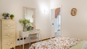 A bedroom with a bed, a dresser, a desk with a chair, a mirror, and a door leading to another room. - Paolino View Apartment (Lucca)