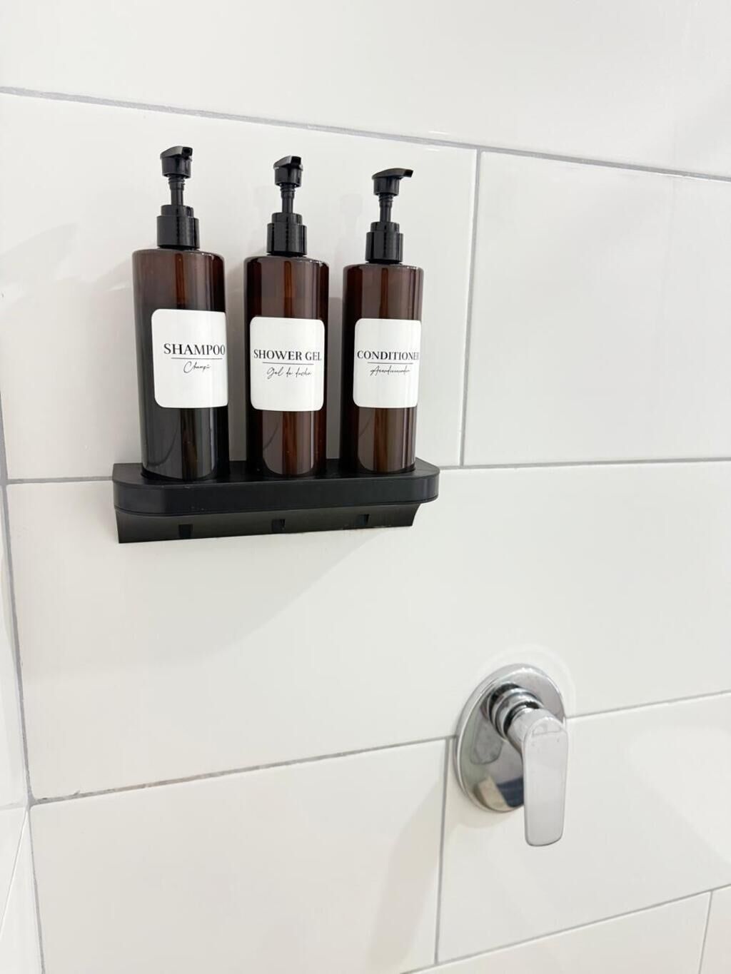 Een badkamer met drie flessen shampoo, douchegel en conditioner op een zwart schap.