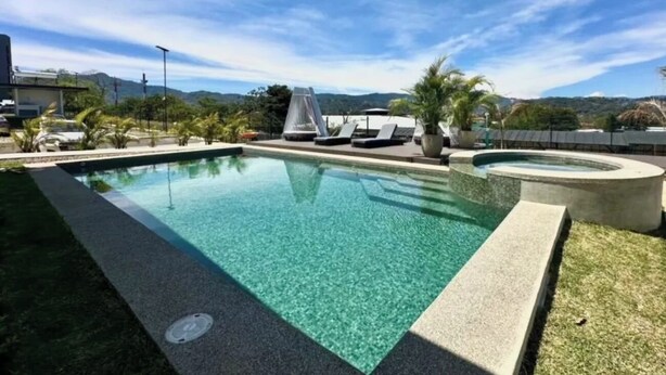 A swimming pool with lounge chairs and a hot tub, surrounded by palm trees and a view of mountains.