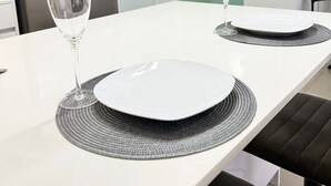 A modern kitchen with a stainless steel refrigerator, a white dining table with two wine glasses and plates, and a bench.
