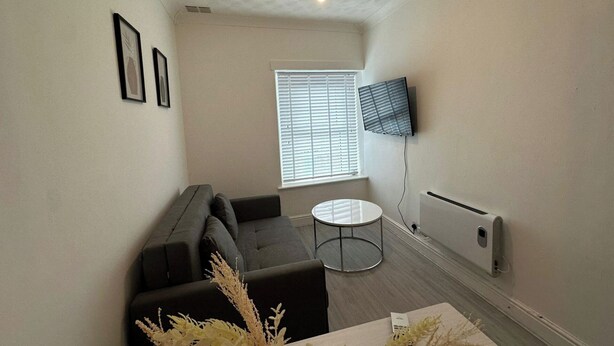 A small, modern living room with a grey sofa, a round coffee table, and a TV mounted on the wall.