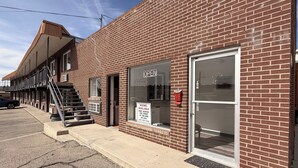 A brick building with a large glass door, a staircase leading to an upper level, and a sign indicating rooms are available for rent.