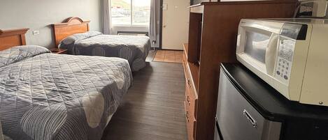 A compact hotel room with two beds, a microwave, and a small kitchenette.