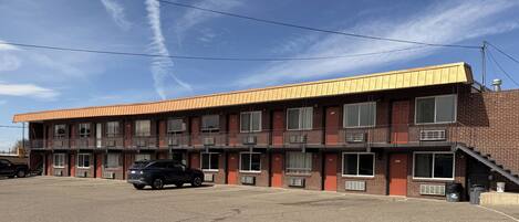 A multi-story motel with a flat roof, multiple windows, and a parking lot.
