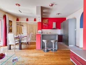 A modern kitchen with a red accent wall, a dining area with white chairs, and a glass table. - Morski dragulj by Interhome (Vodice)