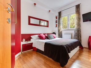 A bedroom with a bed, a nightstand, a dresser, a window with curtains, a wall-mounted TV, and a red door. - Morski dragulj by Interhome (Vodice)