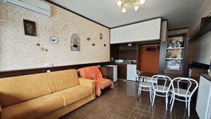 A compact living space with a sofa, dining table, chairs, a kitchenette, and a small kitchen area.