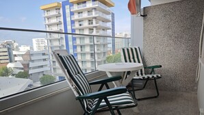 A balcony with two striped chairs and a small round table, overlooking a cityscape with modern buildings.