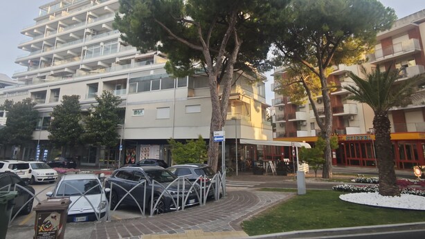 A multi-story hotel with balconies, a parking area with cars, and a restaurant in the foreground.