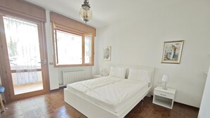 Een slaapkamer met een groot bed, een nachtkastje, een radiator en een raam met jaloezieën.