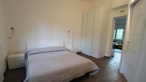 Ein Schlafzimmer mit Bett, Nachttisch, Kleiderschrank und einer Tür zu einem anderen Raum.