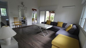 Ein modernes Wohnzimmer mit einer Couch, einem Couchtisch und einem Sessel. Ein Fenster bietet Blick auf grüne Natur.