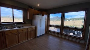 Une cuisine dotée de meubles en bois, d’un réfrigérateur blanc et de grandes fenêtres offrant une vue sur un paysage montagneux.