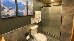 Une salle de bain avec des toilettes, une douche et trois tableaux représentant des paysages accrochés au mur.