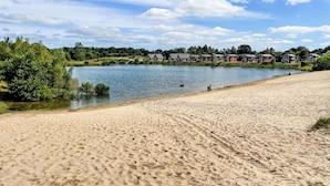 A sandy beach with footprints, a calm lake, and houses in the background. - Geesthof by Interhome (Hechthausen)