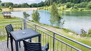 A deck with a table and chairs overlooking a lake, surrounded by trees and a grassy area. - Geesthof by Interhome (Hechthausen)
