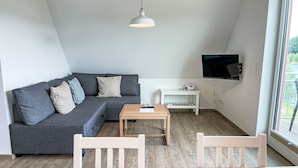 A modern living room with a grey sectional sofa, a wooden coffee table, white chairs, a white TV stand, and a large window. - Geesthof by Interhome (Hechthausen)