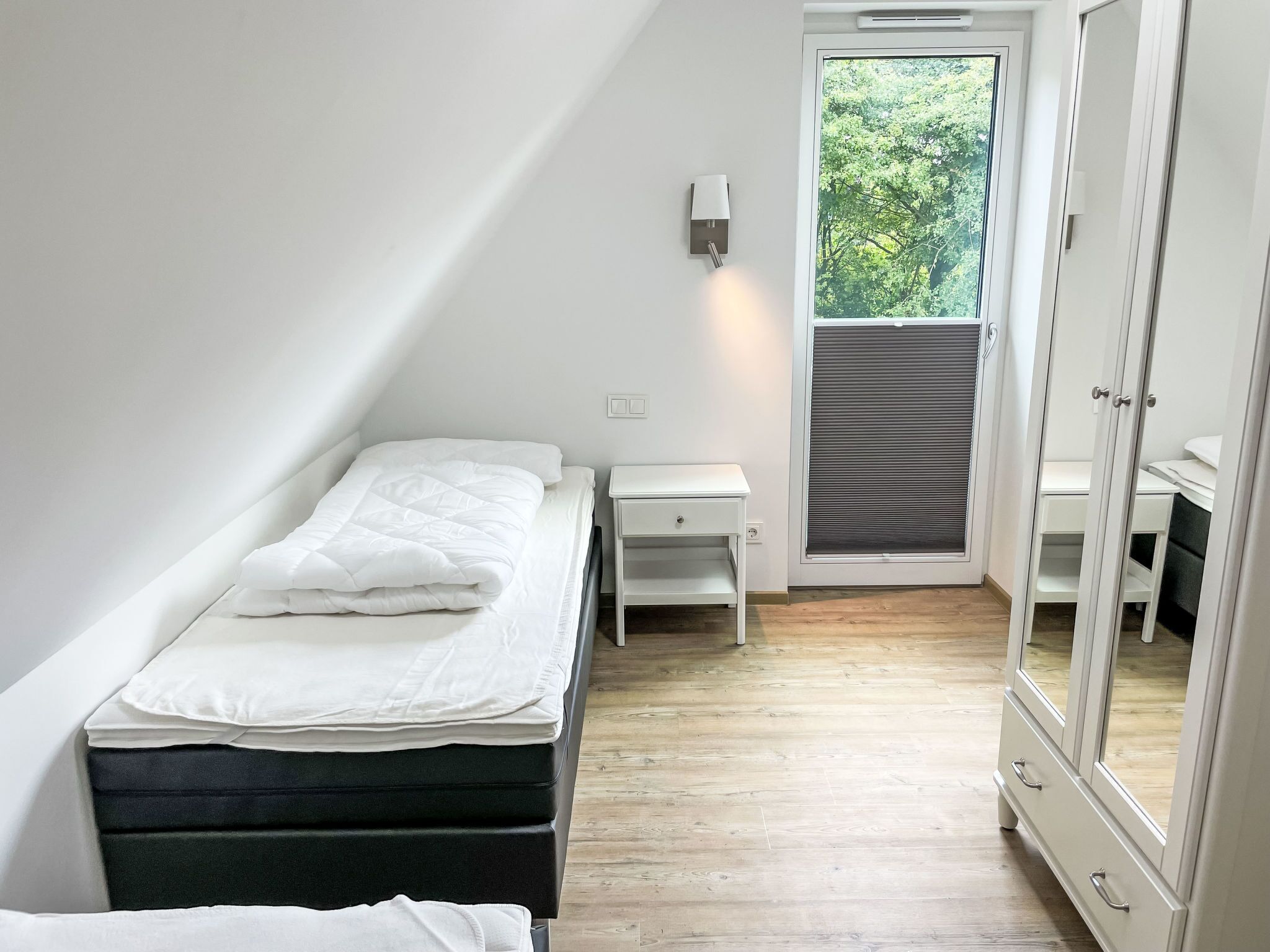 Et lille, godt oplyst soveværelse med en enkelt seng, et natbord, et skrivebord og en garderobe.