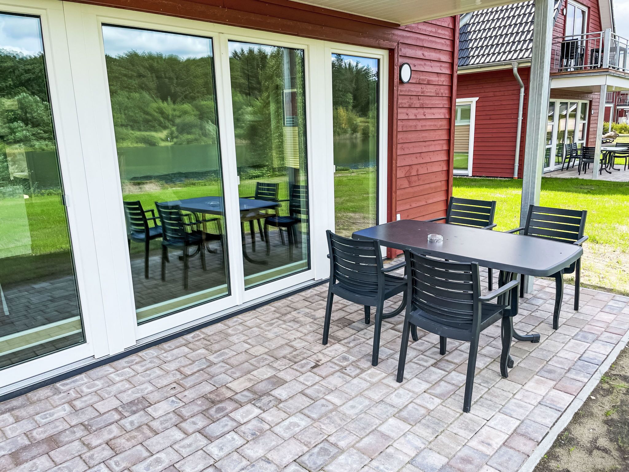 Eine Terrasse mit Tisch und Stühlen, großen Schiebeglastüren und Blick auf eine grüne Landschaft.