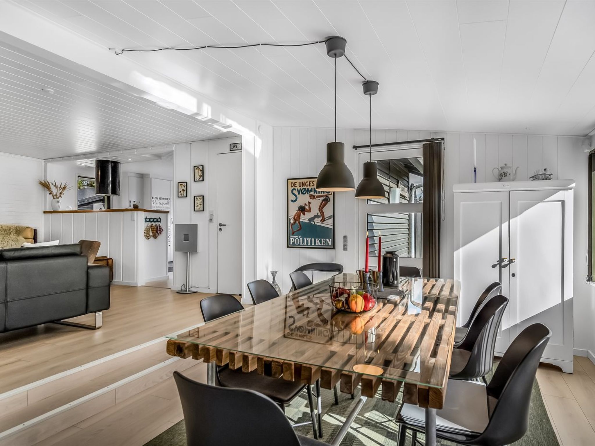 Un espace repas moderne avec une table à plateau en verre, des chaises noires et des luminaires suspendus.