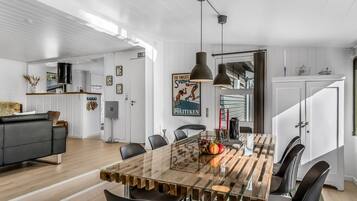 Un espace repas moderne avec une table à plateau en verre, des chaises noires et des luminaires suspendus.