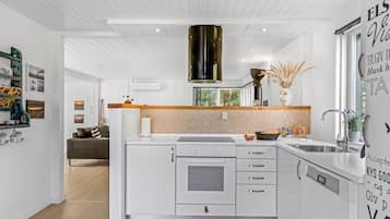 Une cuisine moderne avec des meubles blancs, un plan de travail en bois et un luminaire suspendu noir.