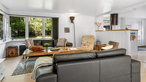 A modern living room with a sofa, armchairs, and a coffee table. There is a large window with a view of greenery outside.