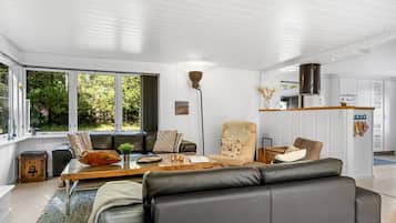 Un salon moderne avec un canapé, des fauteuils et une table basse. Une grande fenêtre offre une vue sur la verdure environnante.