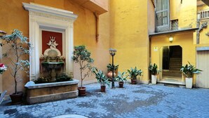 Un patio con una fuente, plantas en macetas y suelo de adoquines.