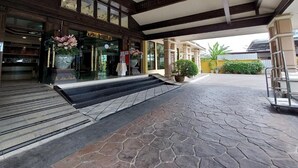A hotel entrance with a stone-paved walkway, a covered area with columns, and a cart. - Ruean Phae Royal Park Hotel (Phitsanulok)