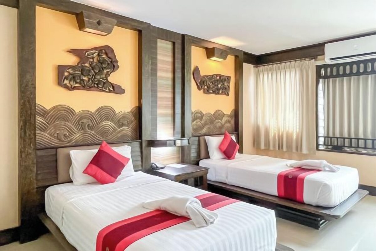 A hotel room with two beds, a wooden headboard, decorative wall art, and a window with curtains.
