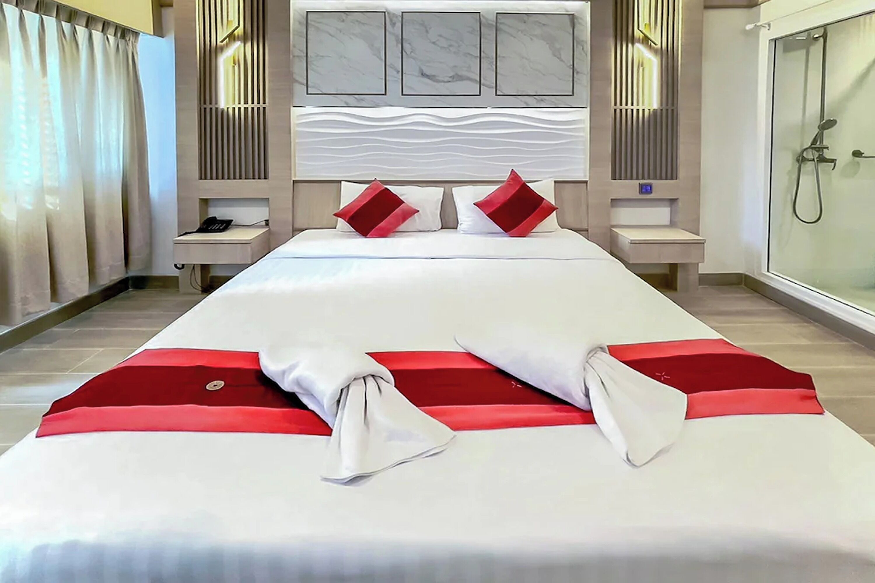 A hotel room with a large bed, two bedside tables, a nightstand, a shower, and a marble headboard.