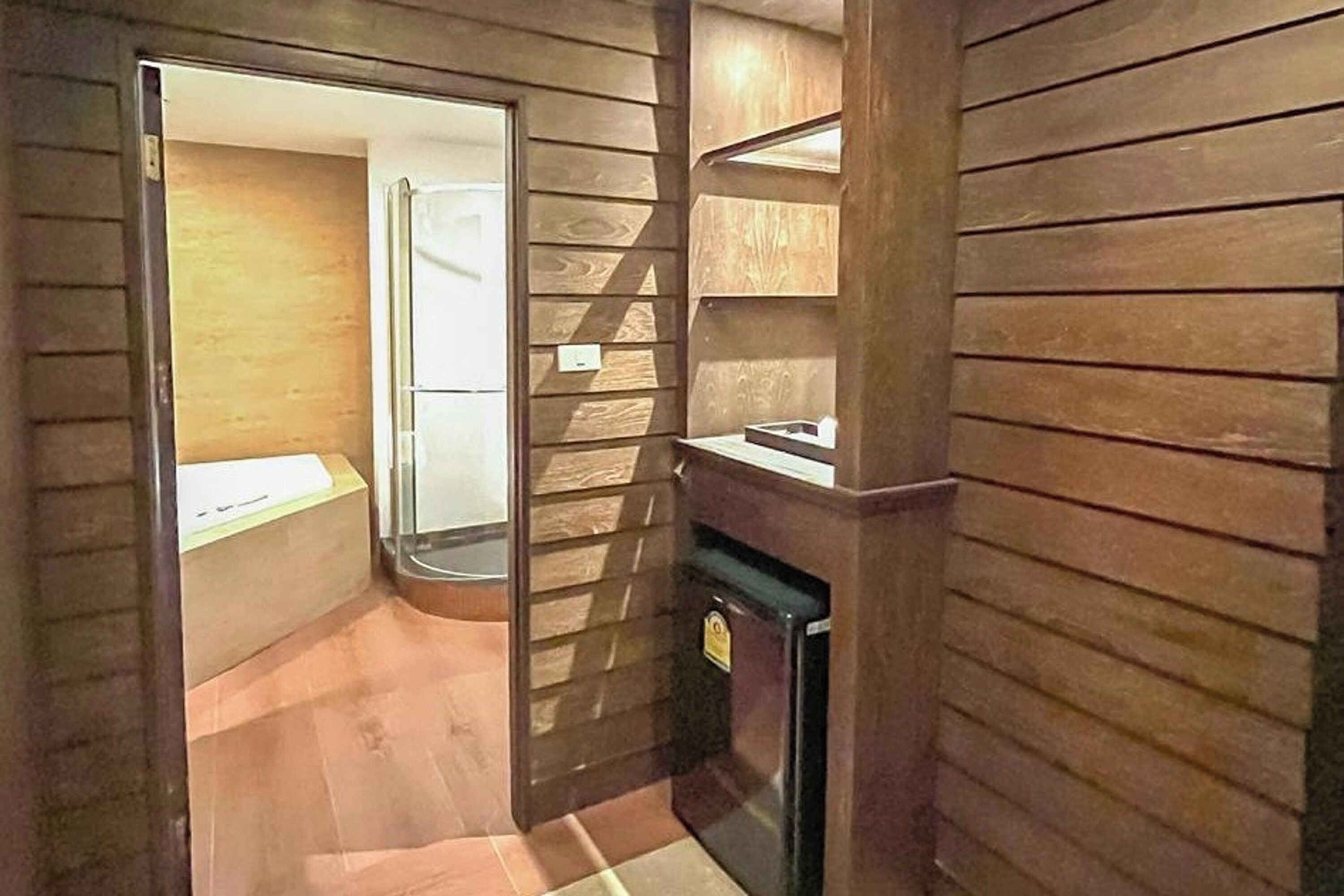 A compact room with wooden paneling, a small refrigerator, and a door leading to another space.