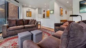 A modern living room with a brown leather sofa, grey ottomans, and a patterned rug. - Palisades Condo – Walk to Ski Lifts, Mtn Views (Tahoe City)