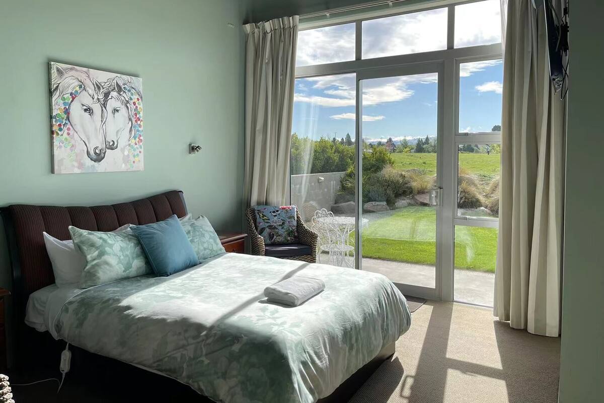 Une chambre avec un grand lit, une chaise et une vue sur un jardin, accessible par une porte-fenêtre coulissante.
